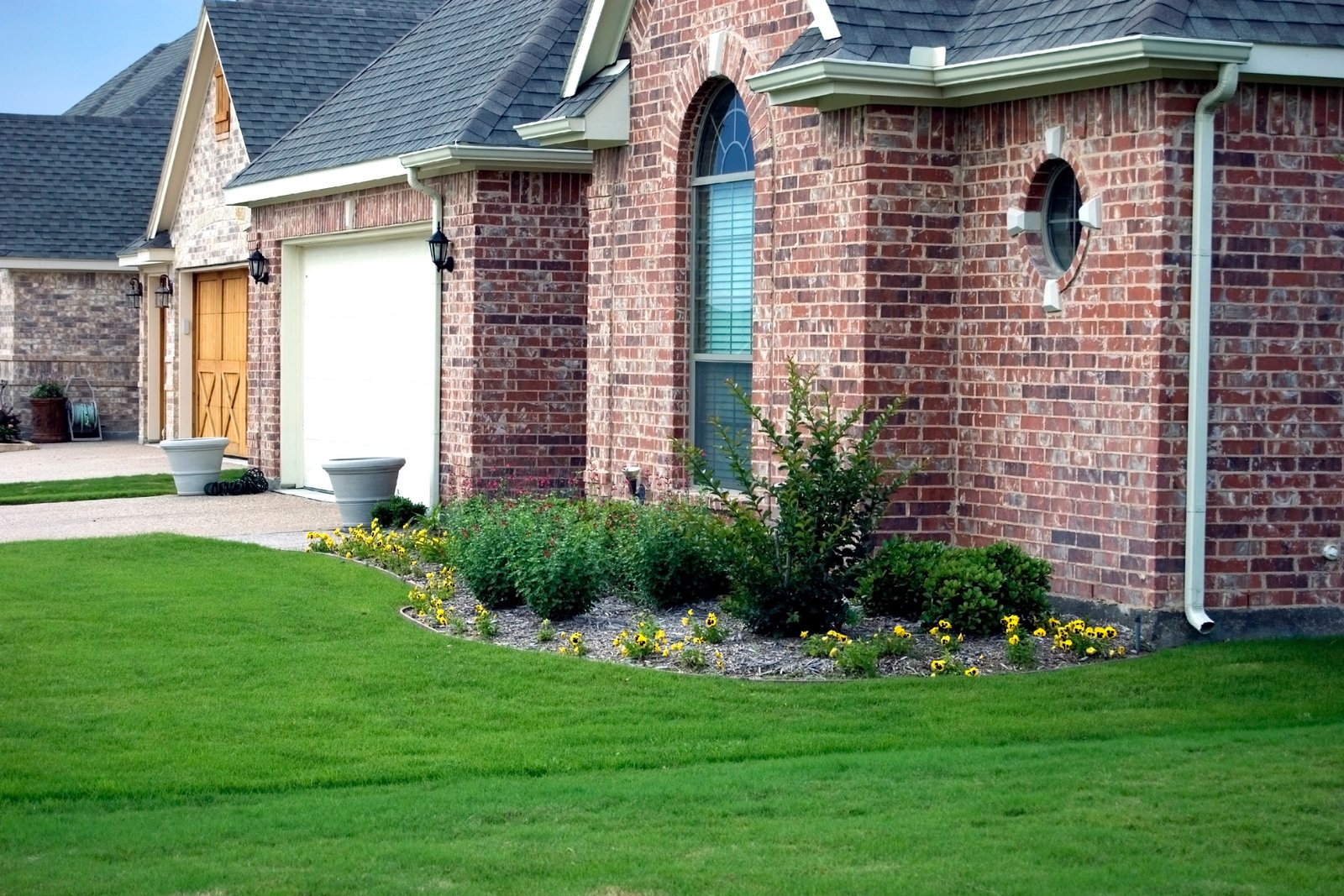 A view of the front elevation of a brick home with white garage doors and lawn flowerbed